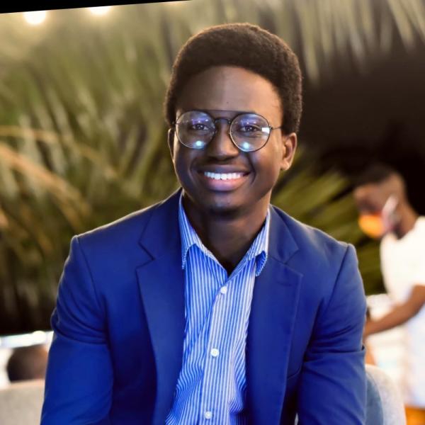 Headshot of Tobi Lafinhan wearing blue jacket and striped blue button up.